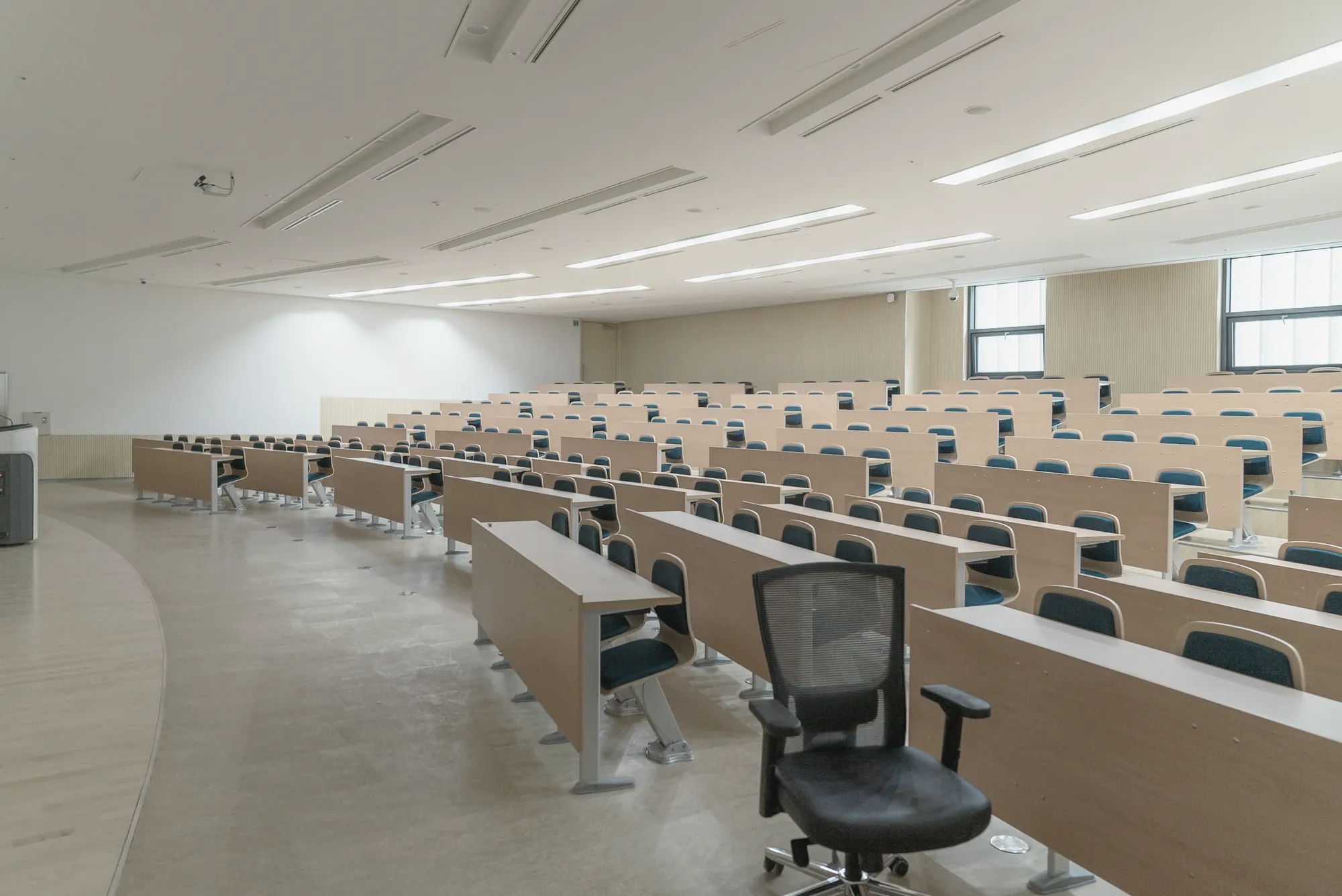 Bright, empty university lecture hall with rows of wooden desks